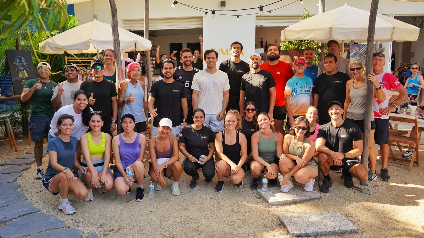 Foto de grupo del Zihuatanejo Run Club: más de treinta corredores reunidos bajo las sombrillas después de la carrera semanal